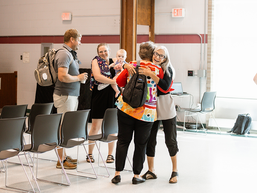 Two women welcoming with hug with family behind